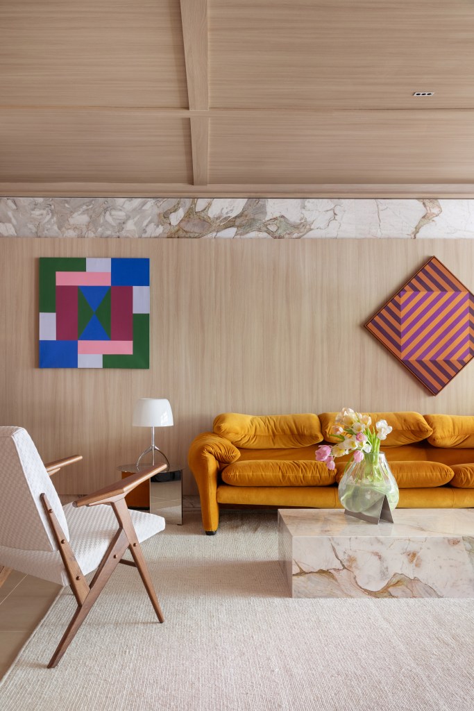 Home office de 45 m² tem estante de marcenaria e mármore e área de estar. Projeto de Rodolfo Consoli para a CASACOR São Paulo 2024. Na foto, sofá terracota, painel de madeira, mesa de centro.