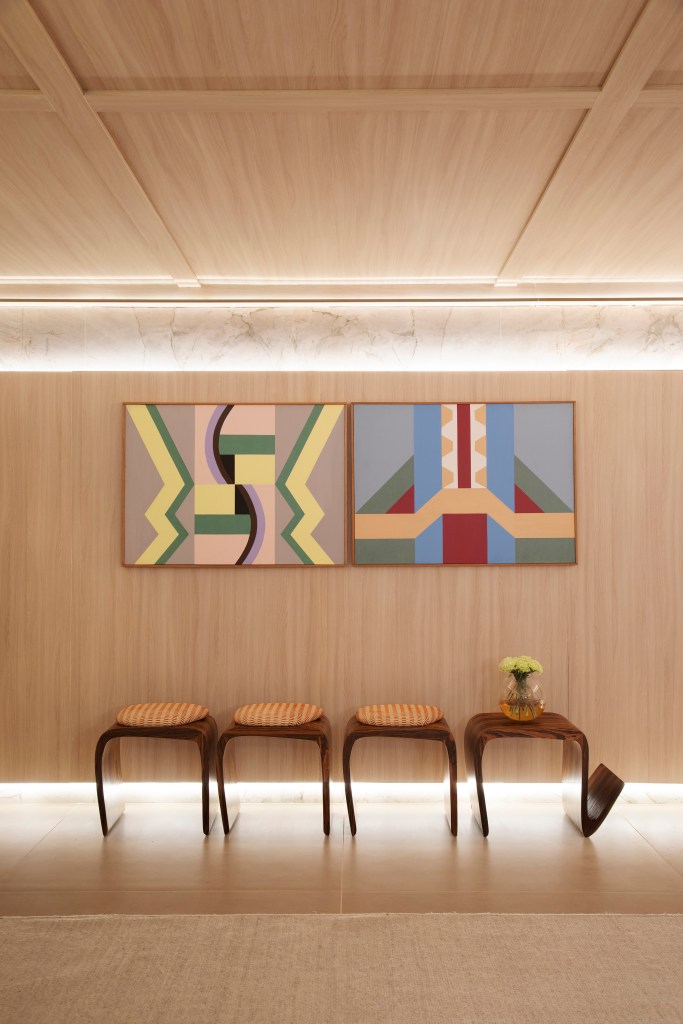 Home office de 45 m² tem estante de marcenaria e mármore e área de estar. Projeto de Rodolfo Consoli para a CASACOR São Paulo 2024. Na foto, painel de madeira, banco, quadros.