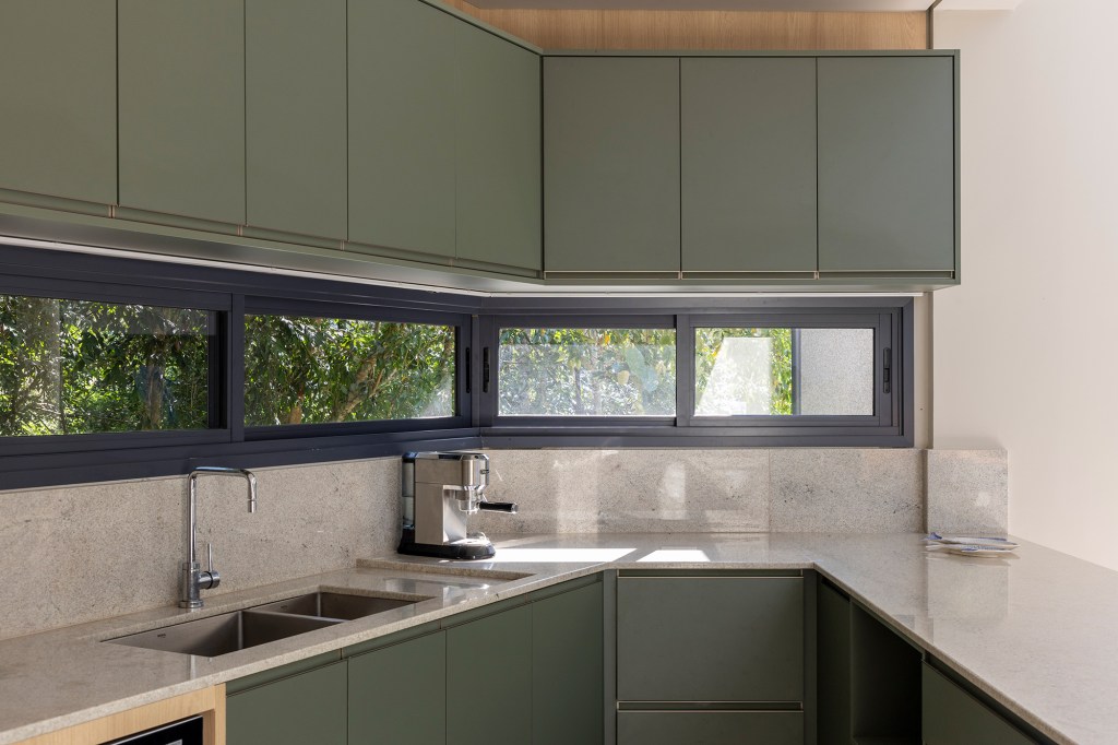 Inspirada no Japão, casa de 524 m² tira proveito da declividade do terreno. Projeto de Cité Arquitetura. Na foto, cozinha com marcenaria verde e vista para as árvores.