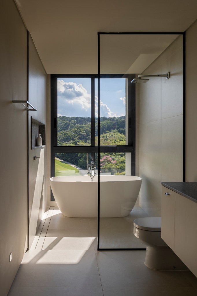 Inspirada no Japão, casa de 524 m² tira proveito da declividade do terreno. Projeto de Cité Arquitetura. Na foto, banheiro com banheira e vista para o verde.