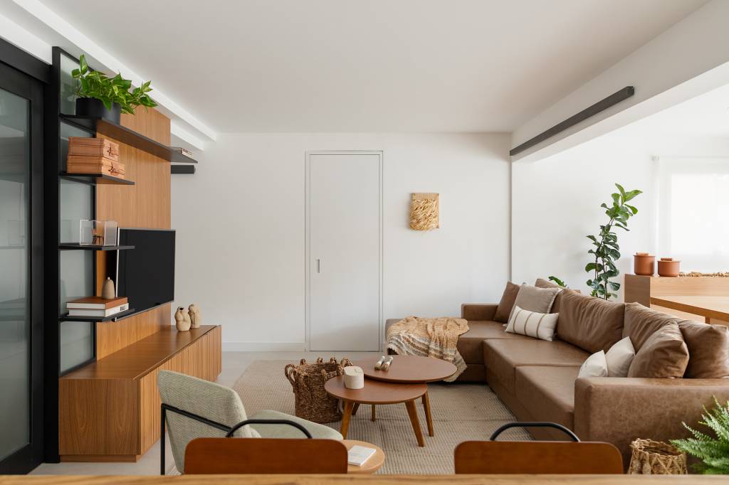 Madeira, conforto e praticidade caracterizam este apartamento de 116 m². Projeto de Studio Canto. Na foto, sala com painel de TV, mesa de centro, tapete e plantas.