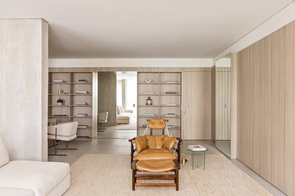 Marcenaria setoriza e decora apartamento de 156 m². Projeto de Alexandre Dal Fabbro. Na foto, sala de estar com paredes ripadas, poltrona e tapete.
