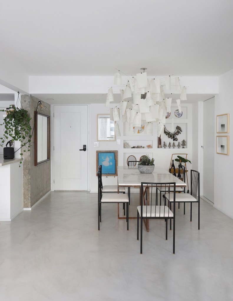 Móveis feitos de alvenaria expõem peças de design em apê de 150 m². Projeto de Rodra Cunha. Na foto, sala de jantar com lustre e mesa branca.