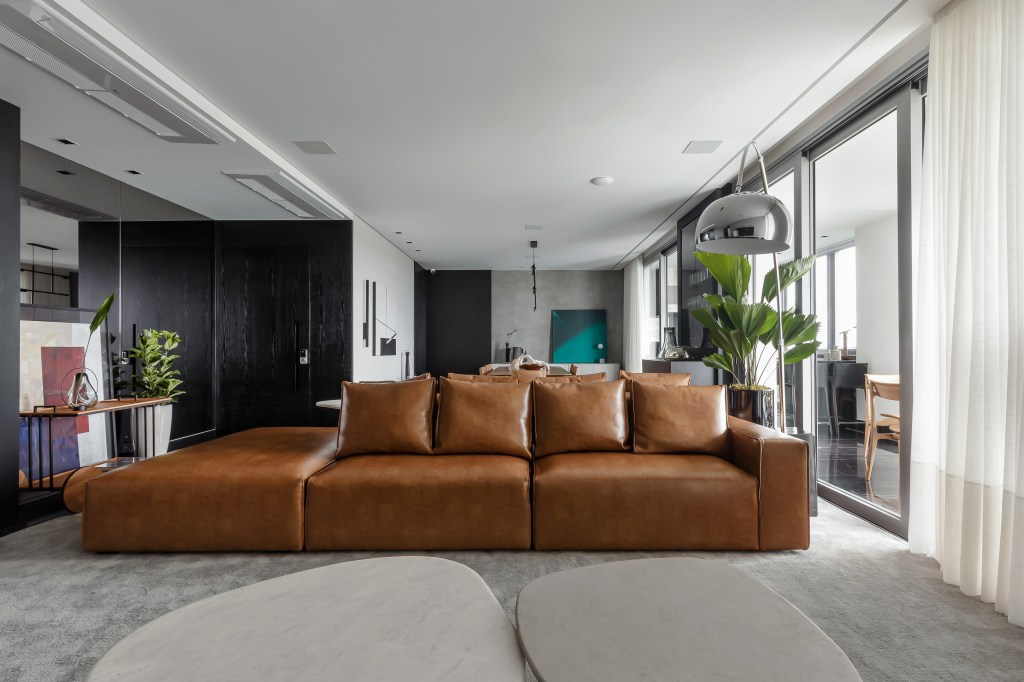 Móveis soltos e paleta sóbria deixam apê de 190 m² atemporal e elegante. Projeto de NK Arquitetura. Na foto, sala de estar integrada, sofá de couro bege.