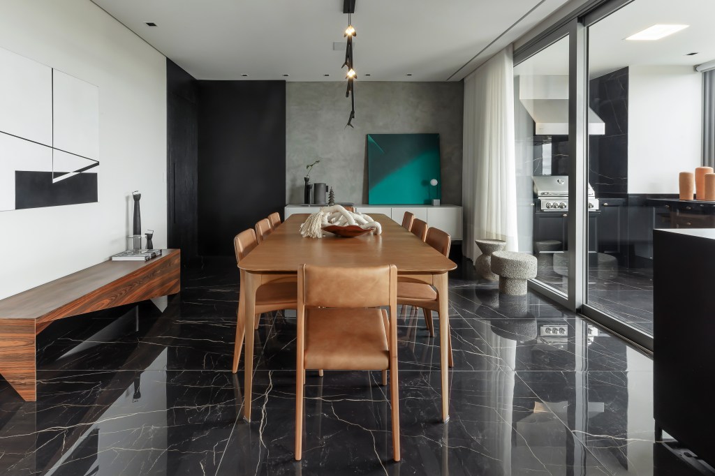Móveis soltos e paleta sóbria deixam apê de 190 m² atemporal e elegante. Projeto de NK Arquitetura. Na foto, sala de jantar, piso preto, mesa de madeira, parede de cimento queimado.