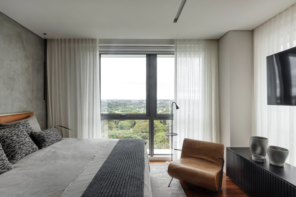 Móveis soltos e paleta sóbria deixam apê de 190 m² atemporal e elegante. Projeto de NK Arquitetura. Na foto, quarto de casal, cortina, poltrona de couro,
