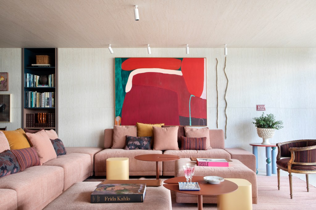Painéis de madeira e tons de rosa criam decoração em homenagem ao feminino. Projeto de Marcelo Salum para a CASACOR São Paulo 2024. Na foto, sofá rosa, quadro, pufes amarelos.