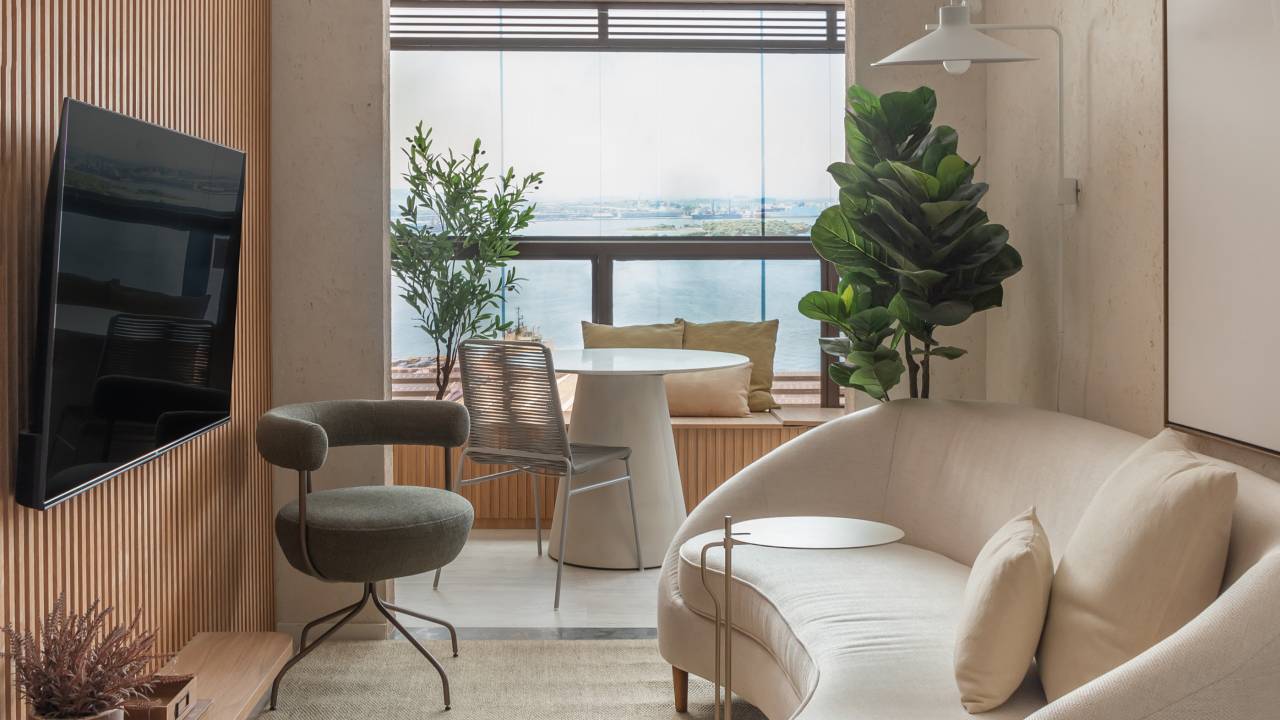 Painéis ripados e tons de bege dão atmosfera serena a apê de 49 m². Projeto de Studio Leandro Neves. Na foto, sala de estar, sofá branco em formato orgânico, tv, tapete bege.