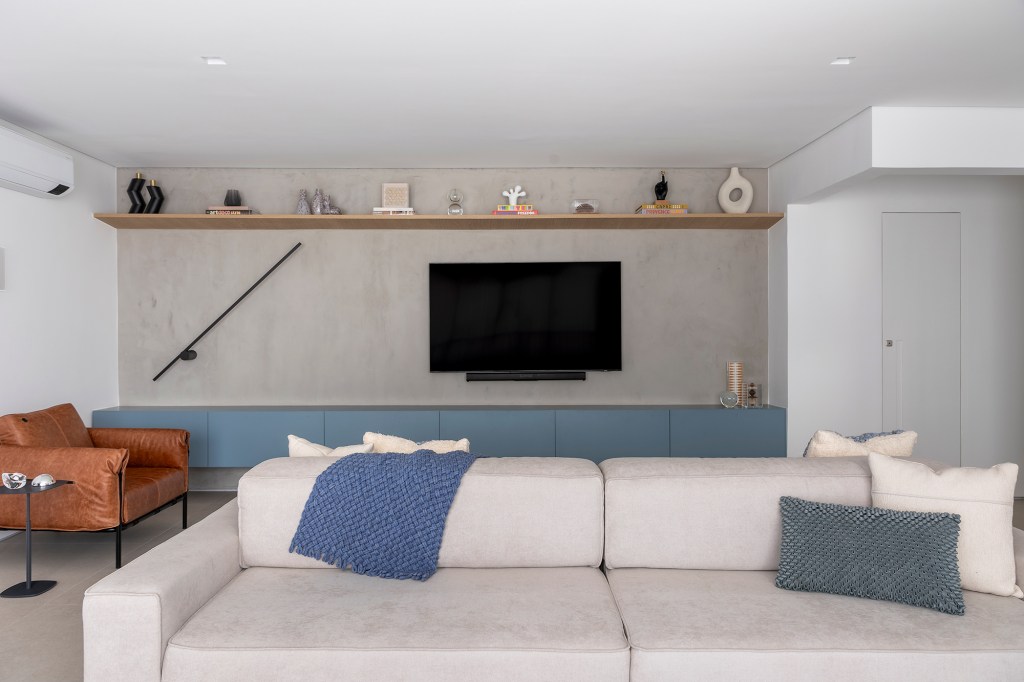 Papel de parede de formiga traz irreverência a este apê de 153 m². Projeto Next Arquitetos. Na foto, sala de estar com TV, rack azul e sofá ilha.