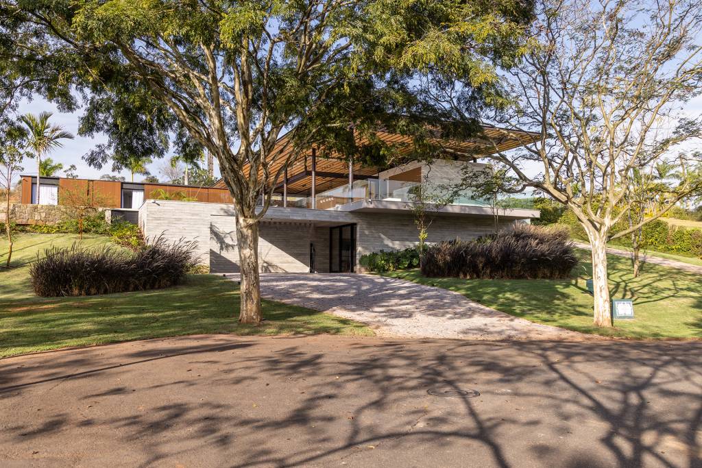 Piscina com muro de pedra dois volumes distintos compõem casa de 700 m². Projeto de Padovani Arquitetos. Na foto, fachada com jardim.