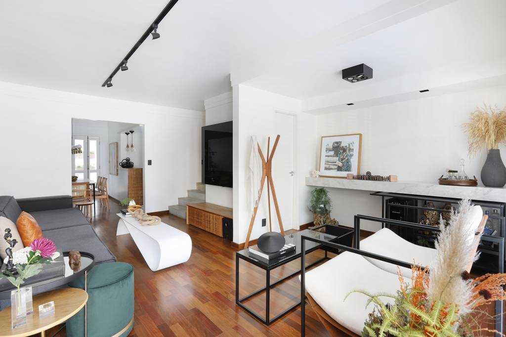 Plantas dentro de casa e jardim na varanda trazem frescor à casa de 200 m². Projeto de Carolina Esper. Na foto, sala com sofá, luminaria e espelho. Aparador com bar e tv.