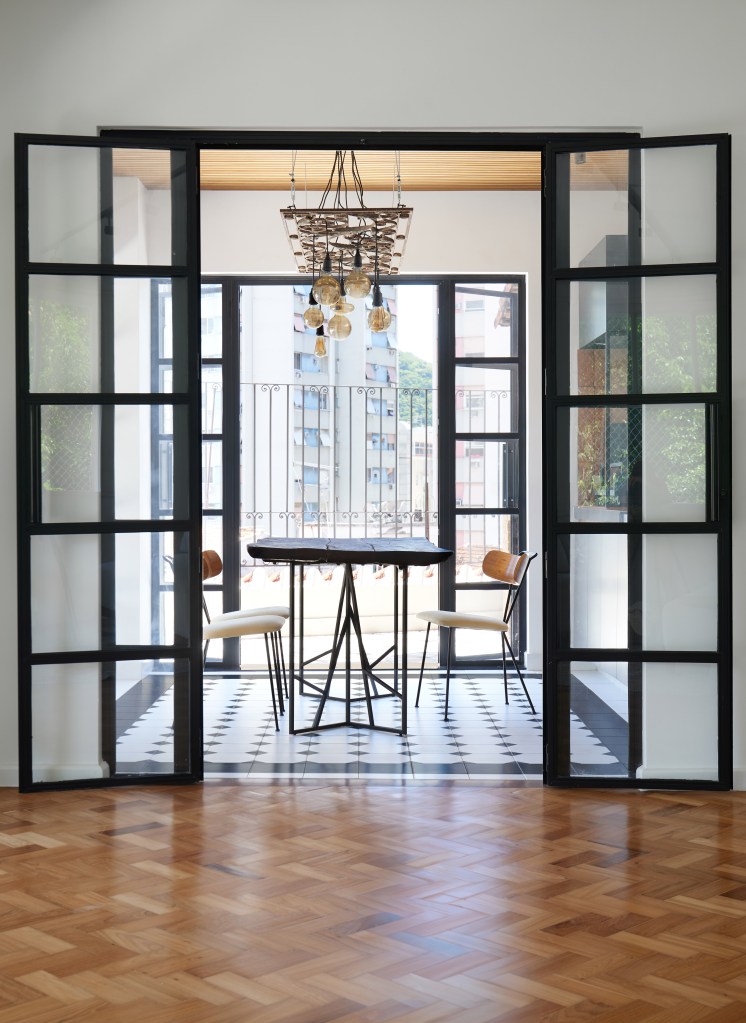 Porta de serralheria vira luminária pendente em cobertura com parrilheira. Projeto de Hugo Rapizo Arquitetura. Na foto, porta de vidro com moldura preta, piso de ladrilho preto e branco, área gourmet.