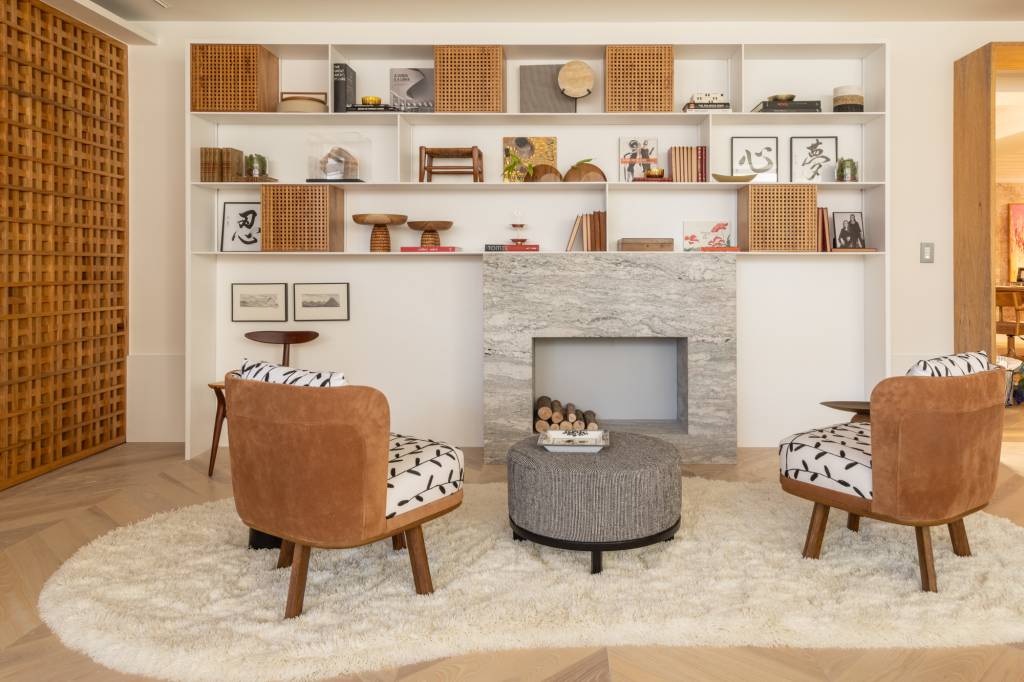 Quarto com conforto de hotel é inspirado na cultura japonesa. Projeto de Migs Arquitetura para a CASACOR SP 2024. Na foto. sala de estar com lareira e poltronas. Prateleiras com livros.