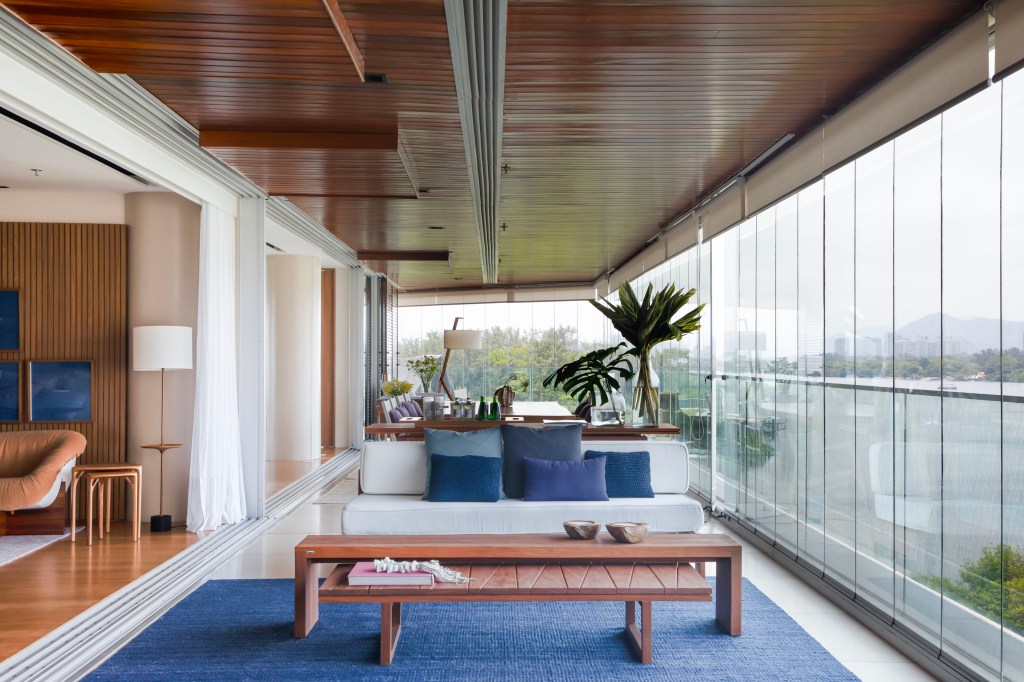 Reforma une dois apês e cria varanda integrada com 34 m lineares de vista. Projeto de Renata Xavier. Na foto, sofá branco, almofadas azuis, tapete azul.