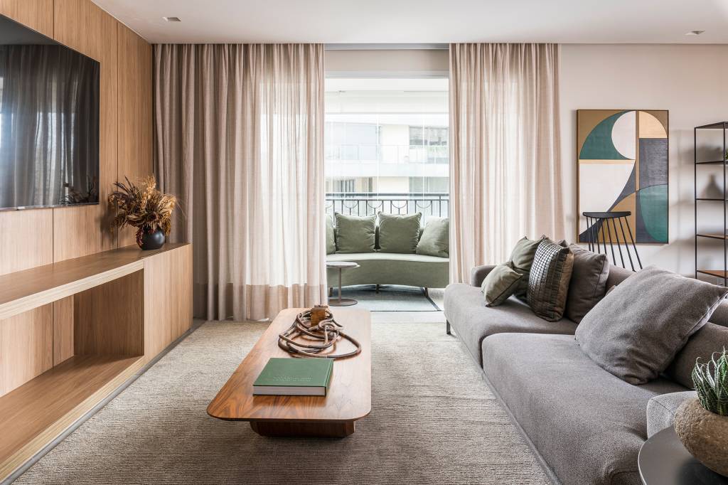 Em um mês, apê alugado de 156 m² ganha projeto contemporâneo e minimalista. Projeto Estúdio Amadas. Na foto, varanda com sofá curvo verde. Sala com TV, tapete e mesa.