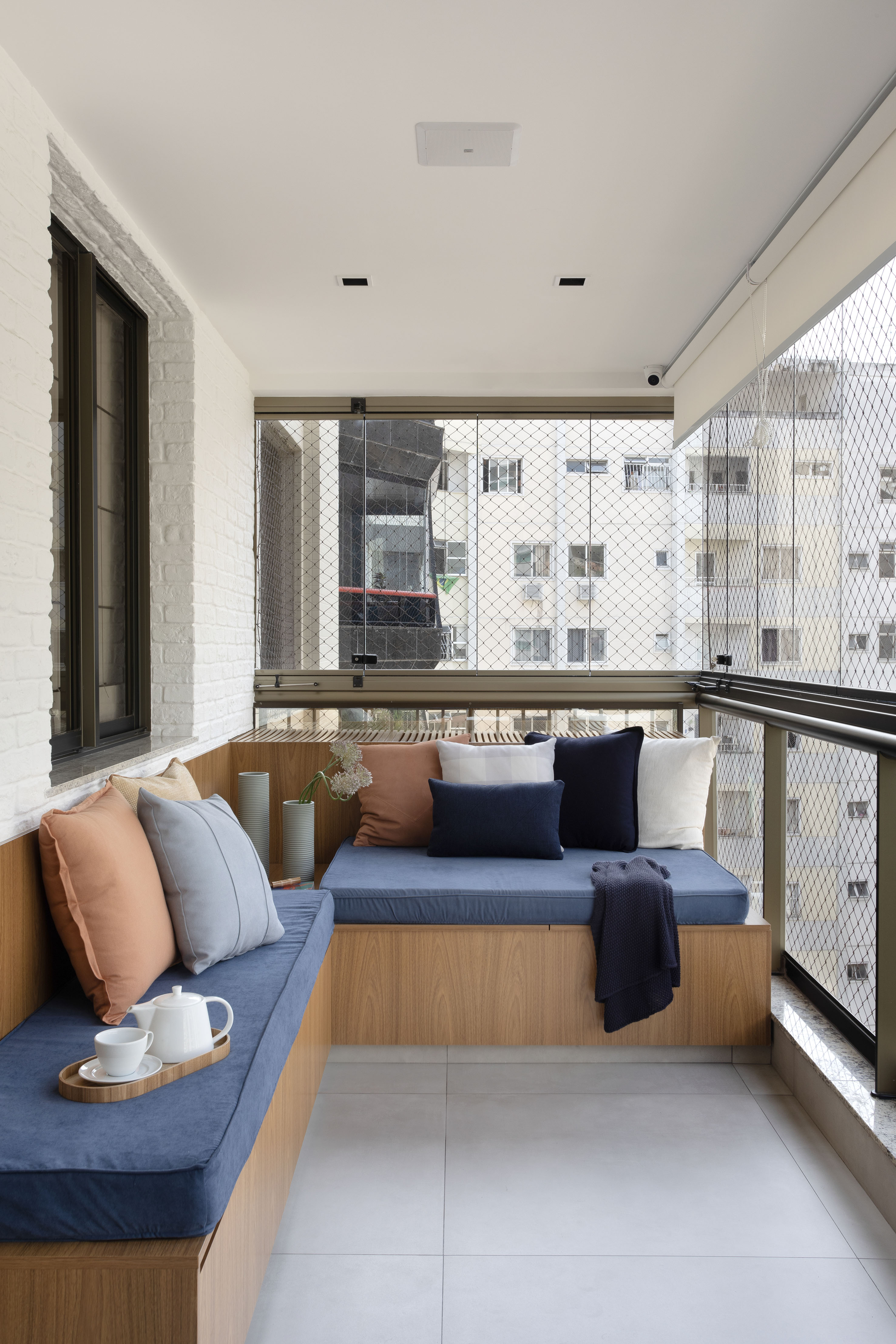 Varanda de 13 m² tem banco-baú, bancada gourmet e piso de porcelanato. Projeto de Travessa Arquitetura. Na foto, banco com baú, futon azul.