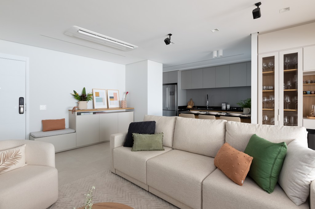 Aconchego e praticidade: apartamento de 126m² possui porcelanato acinzentado neutro e vinílico. Projeto do Estúdio Bena. Na foto, sala de estar integrada com cozinha