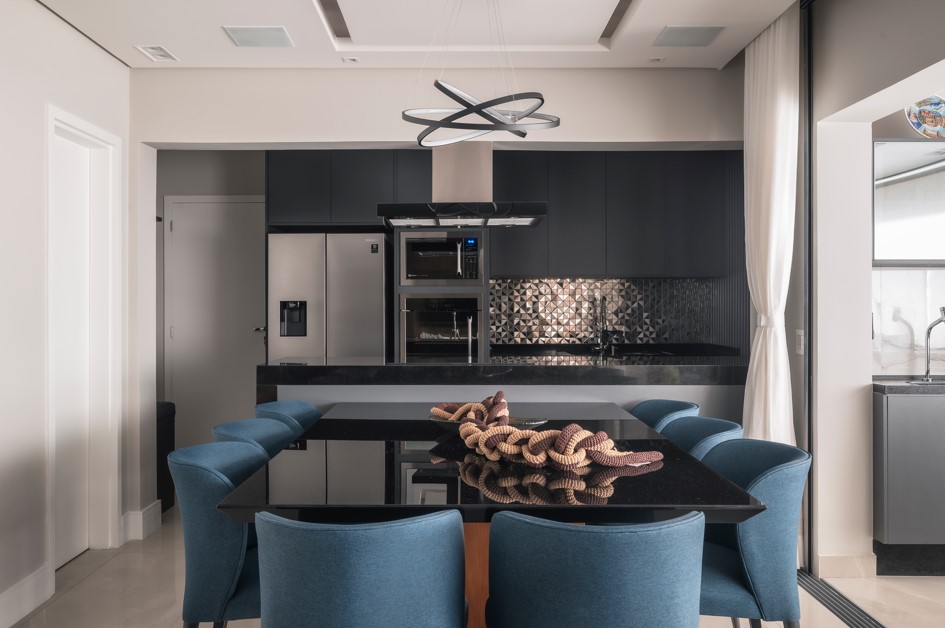 Apartamento de 127 m² tem varanda gourmet e sala com sofá-ilha. Projeto de PB Arquitetura. Na foto, cozinha integrada, mesa de tampo preto, cadeiras azuis.