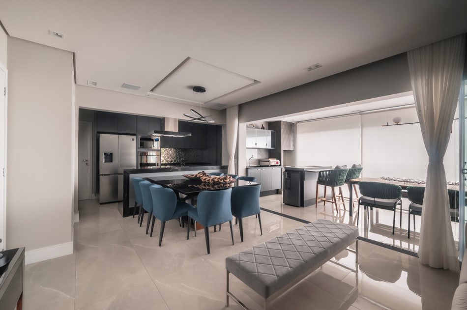 Apartamento de 127 m² tem varanda gourmet e sala com sofá-ilha. Projeto de PB Arquitetura. Na foto, sala, mesa preta, cadeiras azuis.
