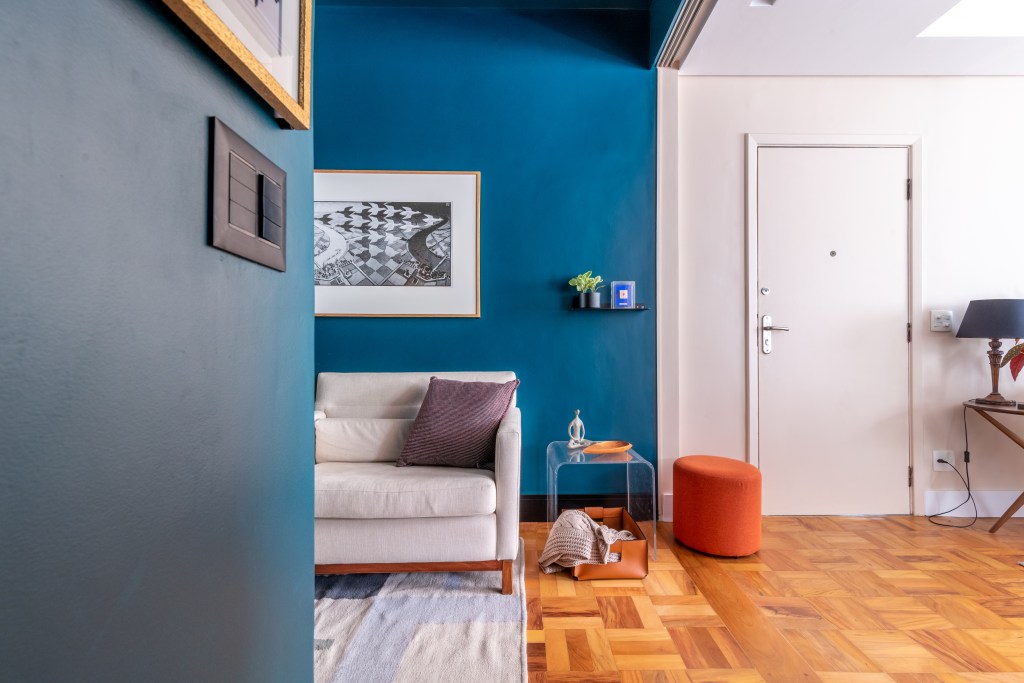 Apartamento térreo ganha brinquedoteca com papel de parede tropical. Projeto de Abrazo Interiores. Na foto, hall, parede azul, sofá cinza, piso de madeira.
