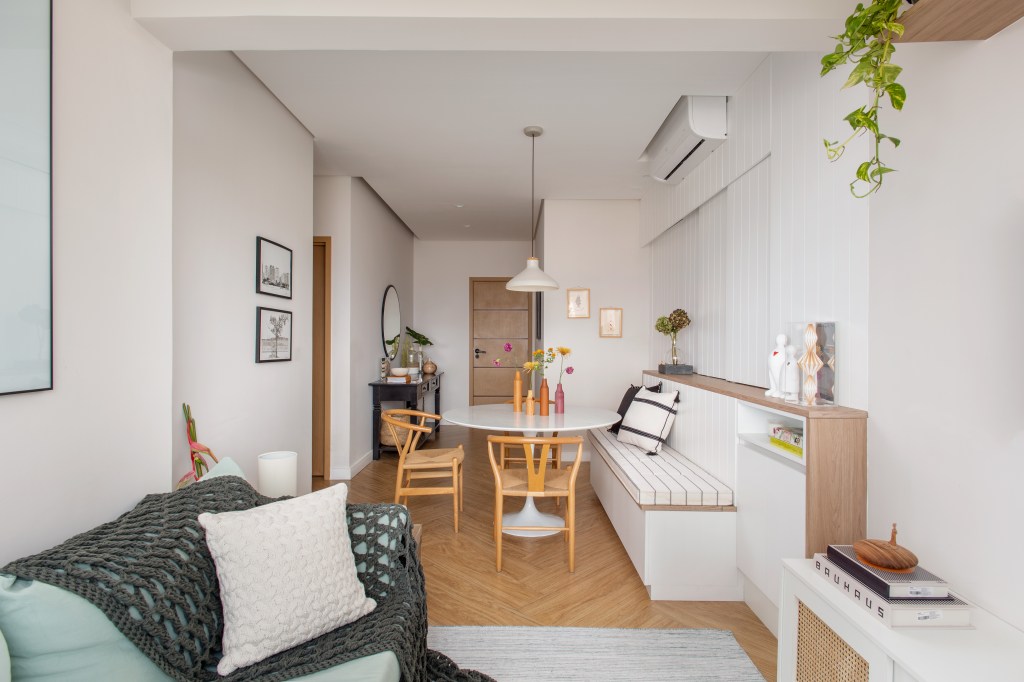 Delicadeza: apê de 66 m² tem cozinha aberta e cabeceira com bordados. Projeto de Memoá Arquitetos. Na foto, sala de estar pequena, banco fixo, ar condicionado.