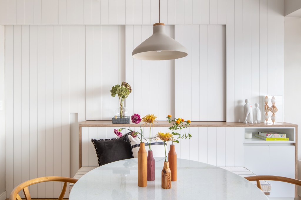 Delicadeza: apê de 66 m² tem cozinha aberta e cabeceira com bordados. Projeto de Memoá Arquitetos. Na foto, cozinha branca com porta de correr de lambri.