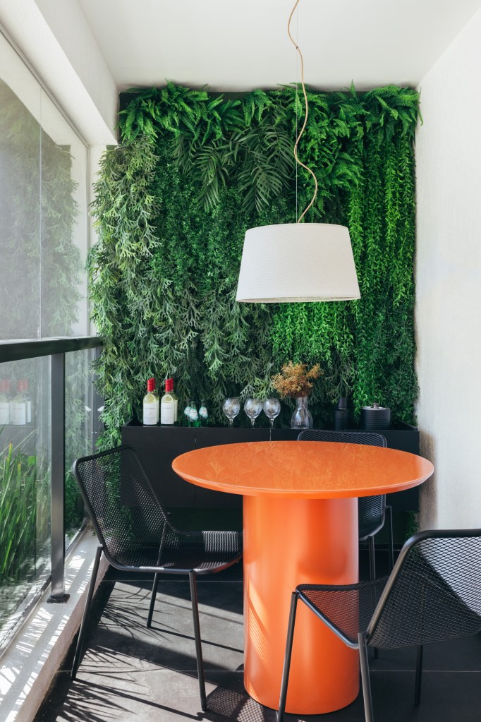 Apê de 73 m² tem marcenaria ebanizada e piso de porcelanato preto. Projeto de Studio Leandro Neves. Na foto, varanda pequena, jardim vertical, mesa laranja.