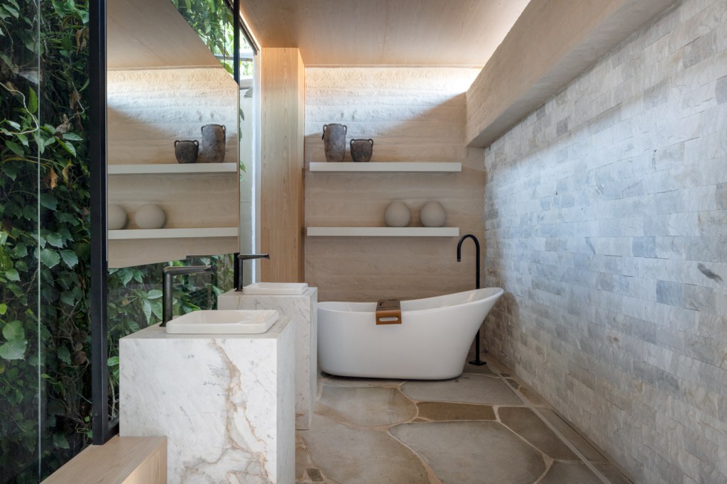 Cabana com telhado de duas águas tem décor escandinavo e lareira. Projeto de GRIFF Arquitetura para a CASACOR Paraná 2024. Na foto, banheiro, jardim vertical, cuba de pedra.