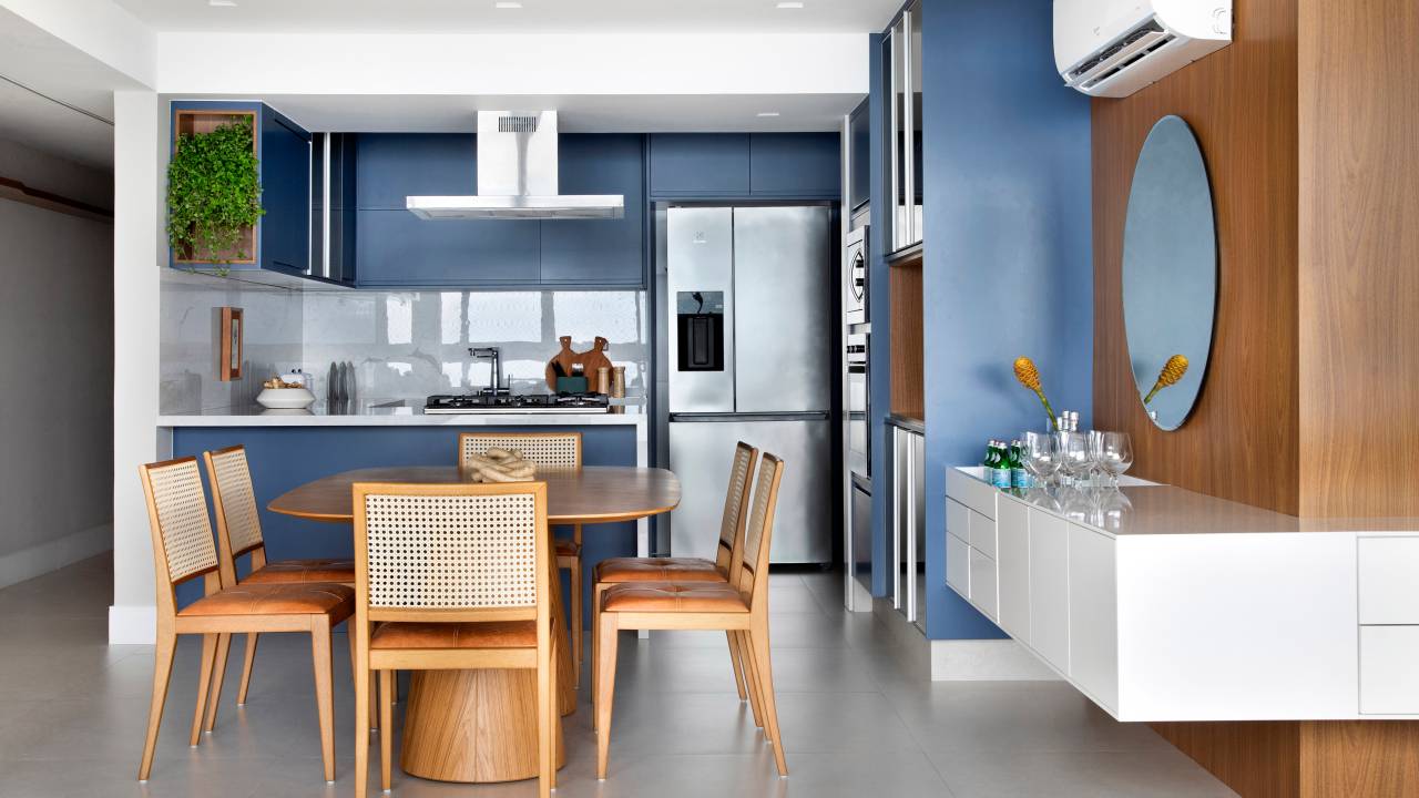 Cozinha com marcenaria em laca azul e MDF tem vista para o mar. Projeto de Travessa Arquitetura. Na foto, sala integrada com cozinha, aparador branco.