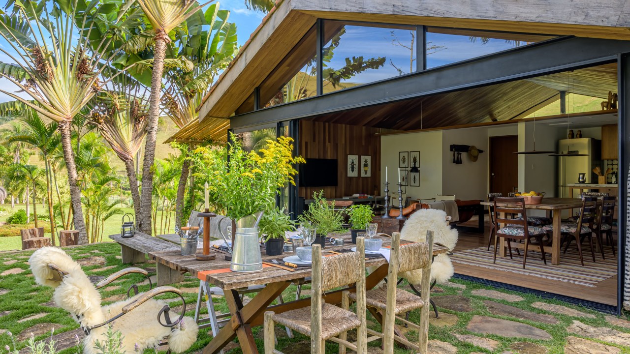 Depósito vira linda cabana no lago de 100 m², com duas suítes e varanda. Projeto de Roberto Souto Interiores. Na foto, jardim, mesa rústica posta.
