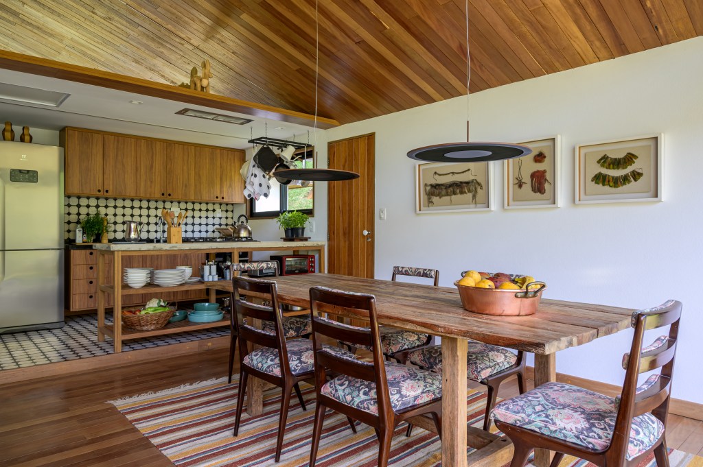 Depósito vira linda cabana no lago de 100 m², com duas suítes e varanda. Projeto de Roberto Souto Interiores. Na foto, mesa de jantar retangular de madeira, tapete listrado.