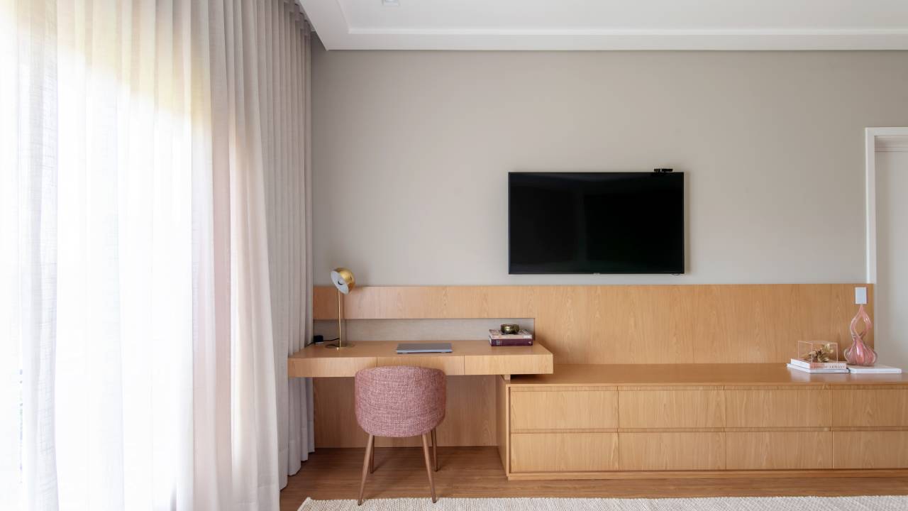 Home office no quarto: arquitetas dão dicas de como compor o ambiente. Projeto de Paiva e Passarini. Na foto, bancada de madeira, cadeira rosa estofada.