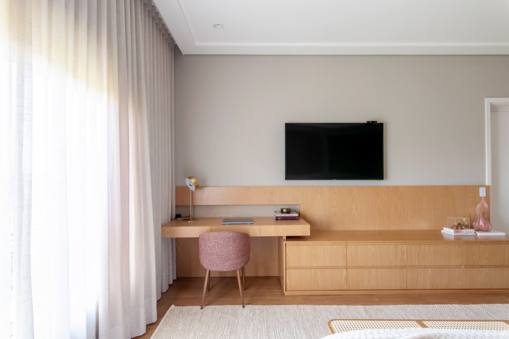 Home office no quarto: arquitetas dão dicas de como compor o ambiente. Projeto de Paiva e Passarini. Na foto, bancada de madeira, cadeira rosa estofada.