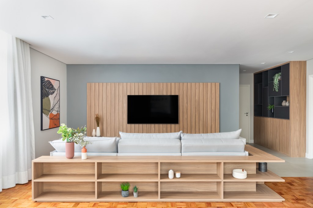 8 ideias para deixar sua sala de estar mais aconchegante. Projeto de Duno Arquitetura. Na foto, painel ripado, tv, aparador atrás do sofá.