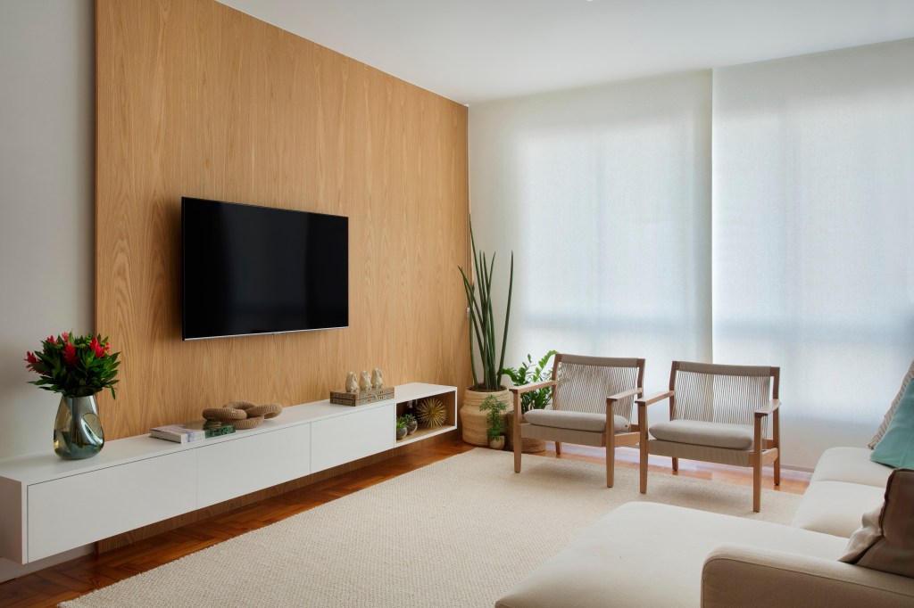 8 ideias para deixar sua sala de estar mais aconchegante. Projeto de Duno Arquitetura. Na foto, sala de estar, painel de madeira, cortina persiana.
