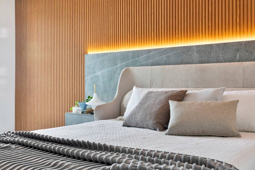 Com paleta ancorada no preto, apê tem painel ripado e piso de porcelanato. Projeto de Rebeca de França. Na foto, quarto, painel dekton, cabeceira, cama.