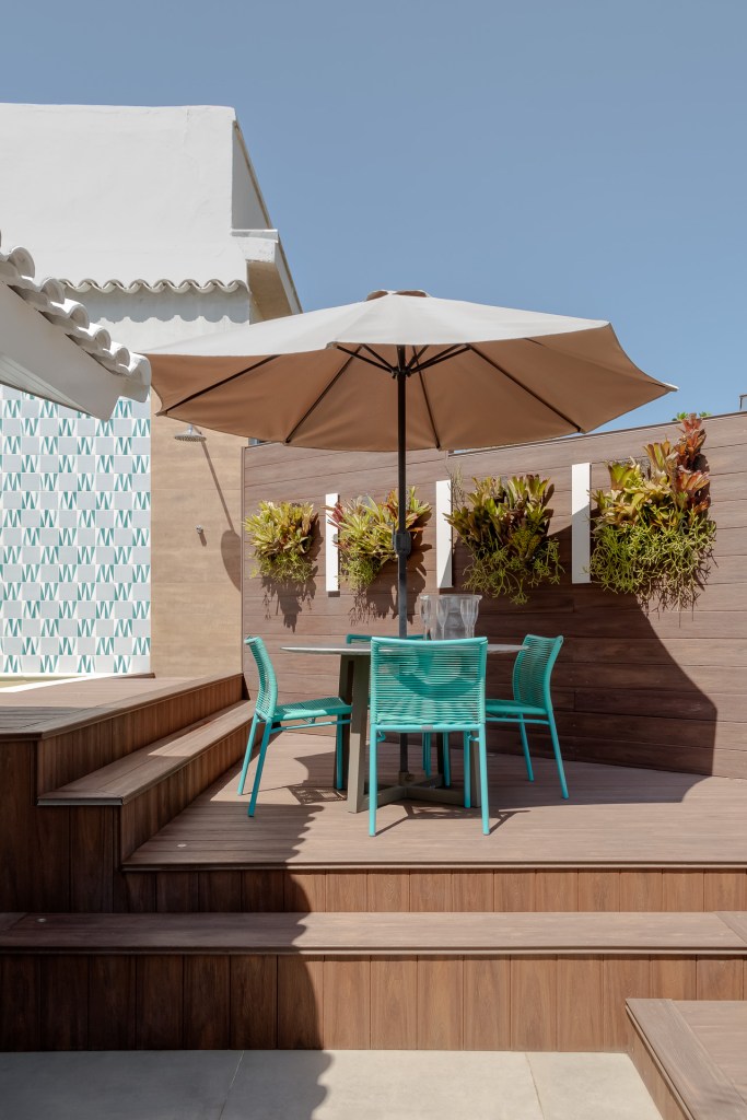 Piscina retangular com deck amplo é centro das atenções em apê de 500 m². Projeto de Ana Cano. Na foto, área externa, ombrelone, jardim vertical pequeno, cadeiras azuis.