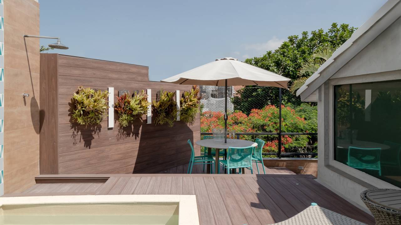 Piscina retangular com deck amplo é centro das atenções em apê de 500 m². Projeto de Ana Cano. Na foto, área externa, ombrelone, jardim vertical pequeno, cadeiras azuis.