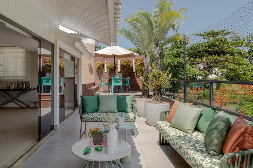 Piscina retangular com deck amplo é centro das atenções em apê de 500 m². Projeto de Ana Cano. Na foto, varanda com sofás e poltronas verdes.