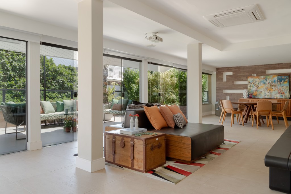 Piscina retangular com deck amplo é centro das atenções em apê de 500 m². Projeto de Ana Cano. Na foto, sala, janelas, sofá baú vintage.