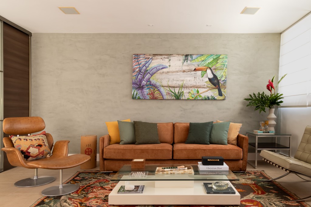 Piscina retangular com deck amplo é centro das atenções em apê de 500 m². Projeto de Ana Cano. Na foto, sala de estar, sofá marrom, almofadas verdes, tapete colorido.