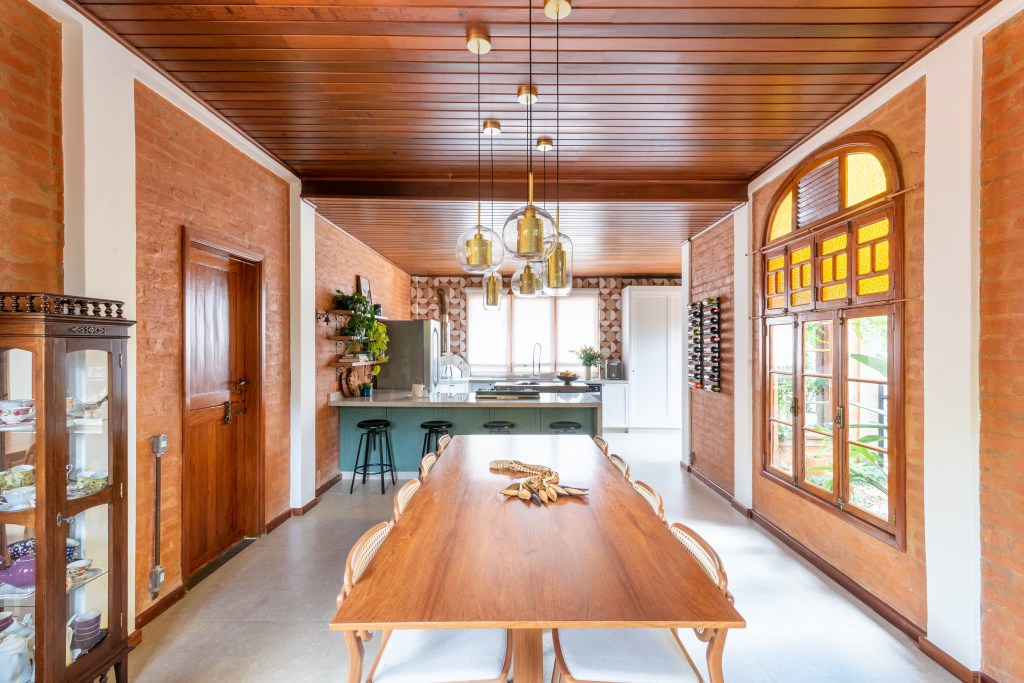 Sobrado de 160 m² em estilo rústico ganha cozinha verde com forno de pizza. Projeto de Abrazo Interiores. Na foto, mesa grande de madeira.