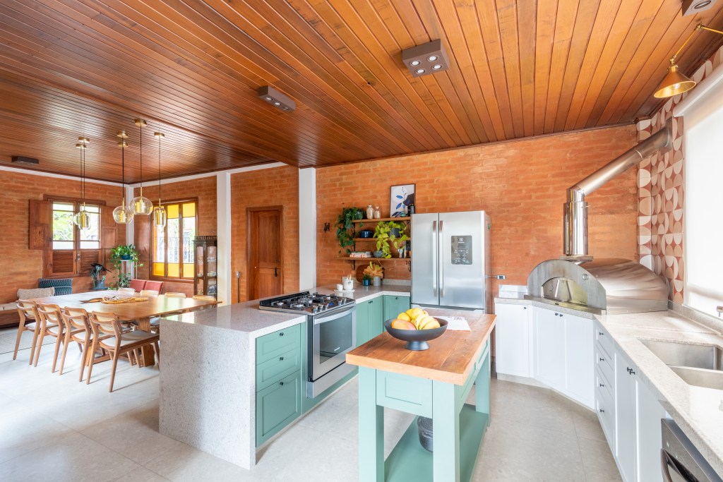 Sobrado de 160 m² em estilo rústico ganha cozinha verde com forno de pizza. Projeto de Abrazo Interiores. Na foto, cozinha, ilha pequena, forro de madeira.