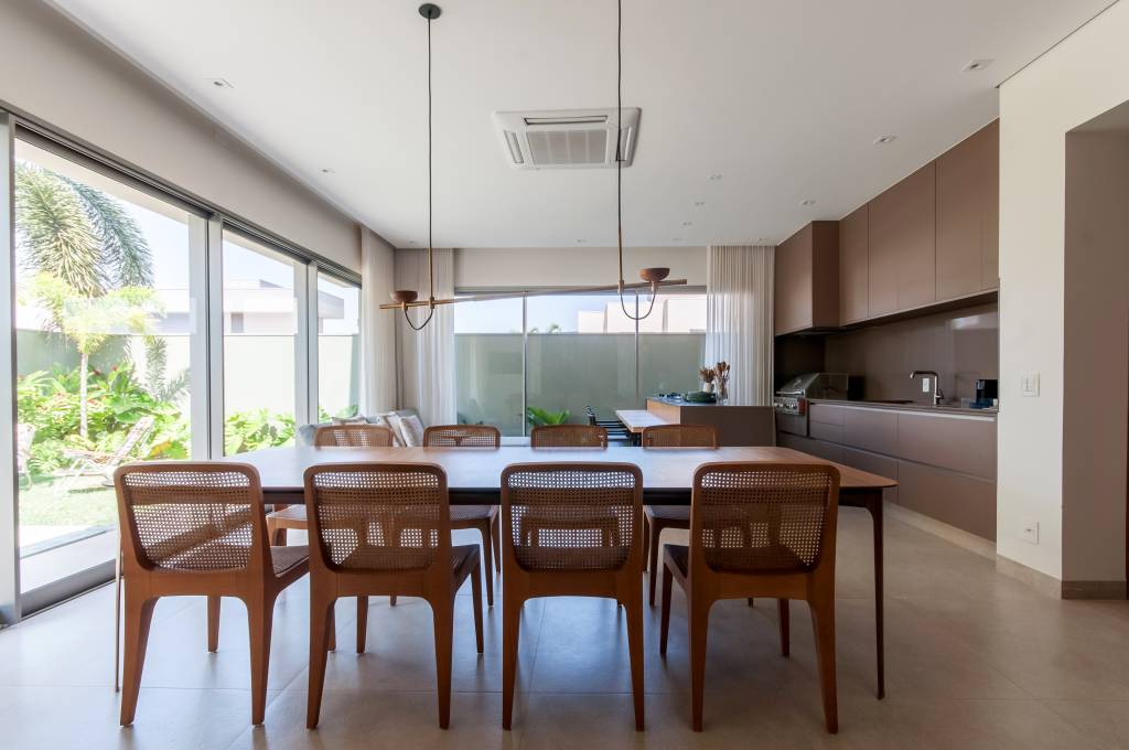 6 tipos de materiais de tampo de mesa para salas de jantar e áreas gourmet. Projeto de Paiva e Passarini Arquitetura. Na foto, mesa com tampo retangular de madeira, cadeiras com encosto de palhinha.