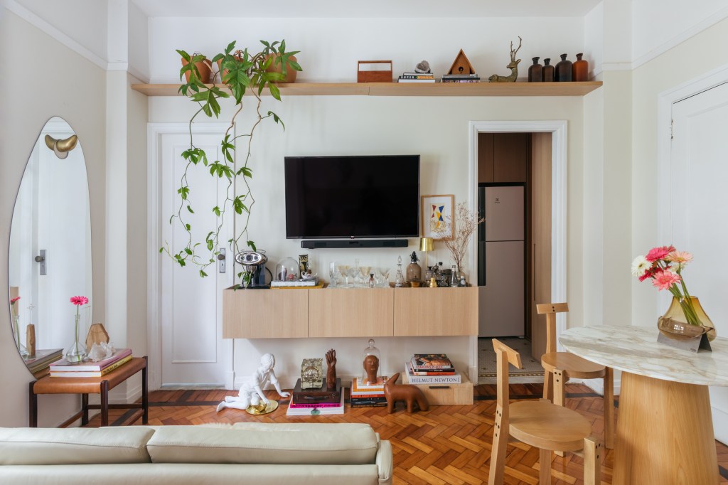 Apê de 42 m² em tons de branco e bege tem sala e quarto integrados. Projeto de Rodolfo Consoli. Na foto, sala de estar, sofá, aparador aéreo, prateleira com planta.