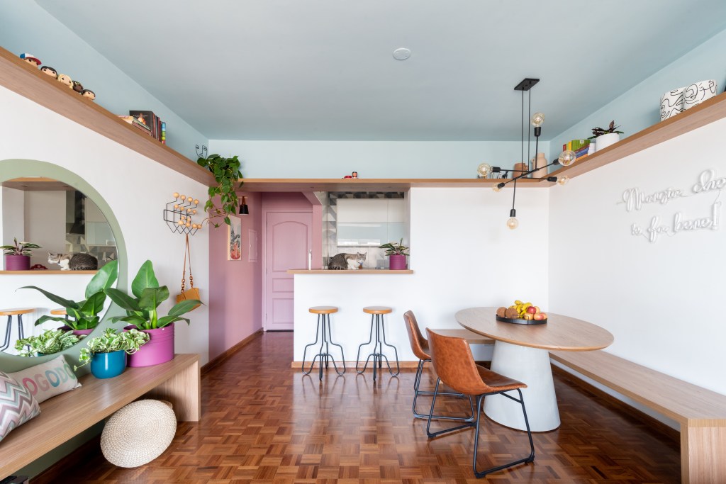 Apê de 72 m² colorido e vibrante tem canto alemão e sapateira no hall rosa. Projeto de Abrazo Interiores. Na foto, sala, mesa redonda pequena, teto colorido.