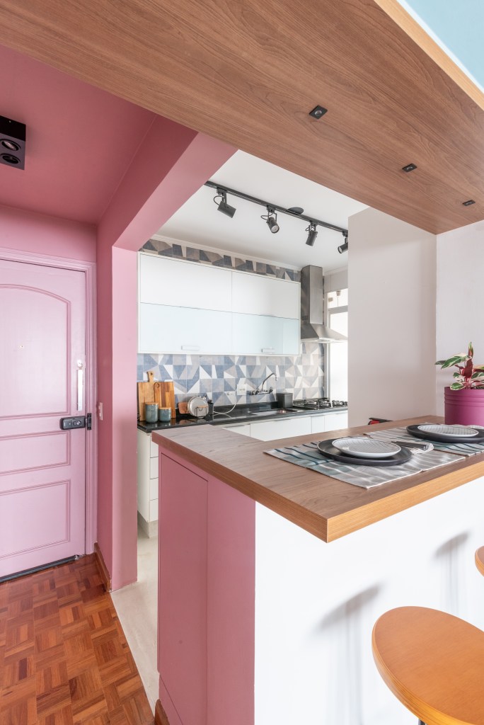 Apê de 72 m² colorido e vibrante tem canto alemão e sapateira no hall rosa. Projeto de Abrazo Interiores. Na foto, cozinha integrada, porta rosa.