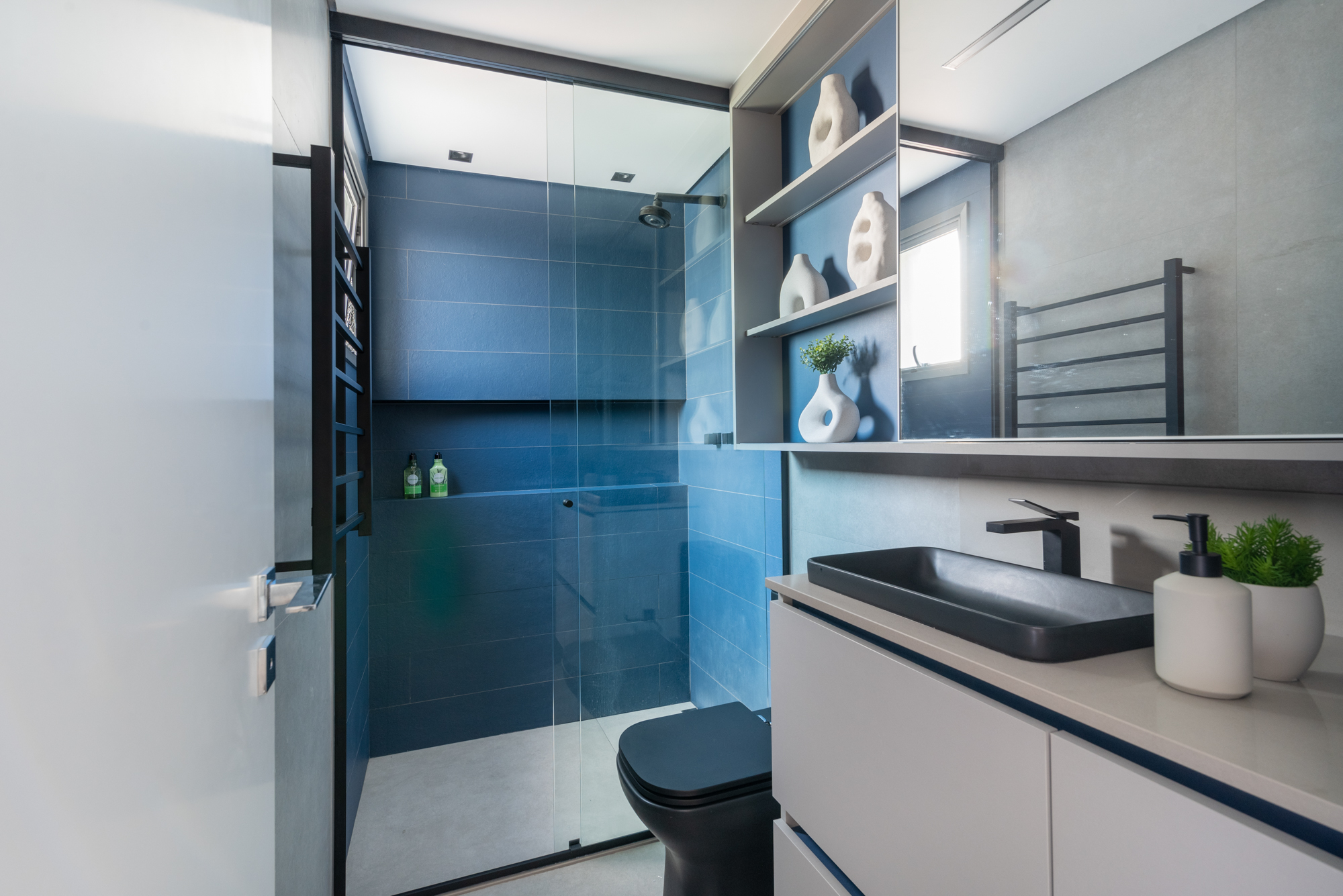Apê de 79 m² tem mesa suspensa na sala de jantar e toalheiro elétrico no banheiro. Projeto de Red Square Arquitetura. Na foto, banheiro com metais pretos e azulejos azuis no box.