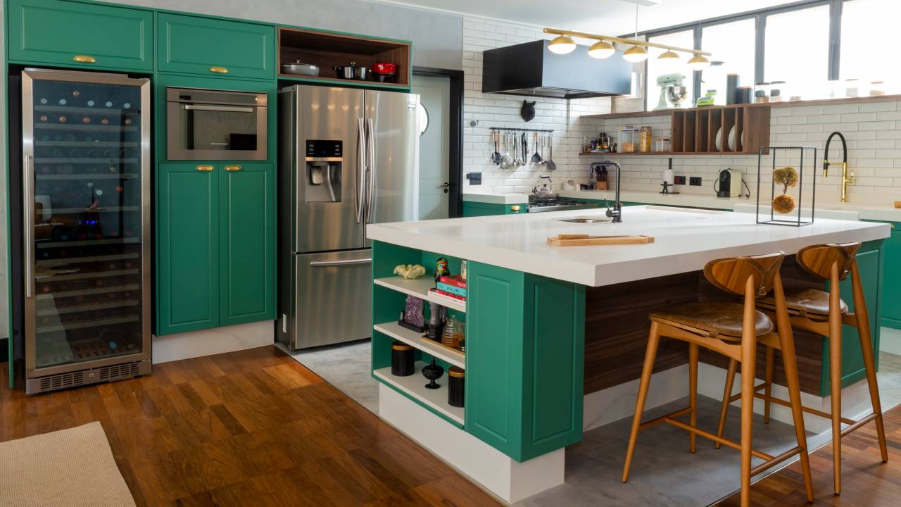 Decoração de apê combina cozinha provençal verde com sala de estar industrial. Projeto de Daniel Szego. Na foto, cozinha com ilha, bancada branca.