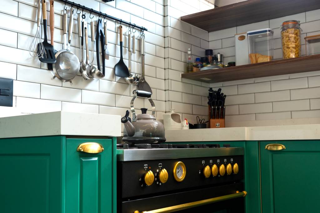 Decoração de apê combina cozinha provençal verde com sala de estar industrial. Projeto de Daniel Szego. Na foto, cozinha, bancada branca, subway tiles, utensílios pendurados.